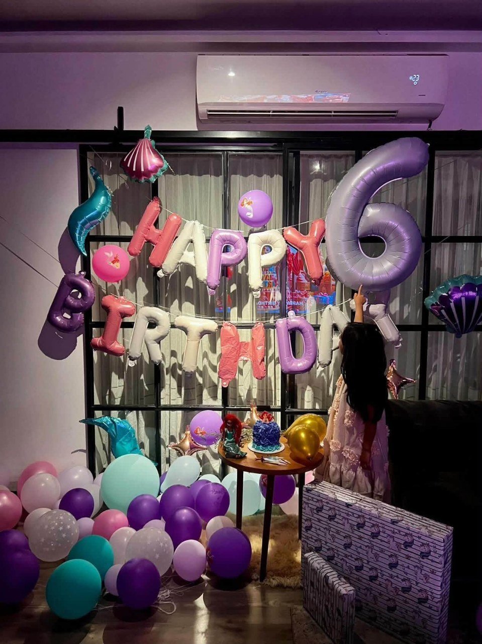 Mermaid themed sixth birthday setup with pastel pink, lilac and teal balloon letters, a large lilac number 6 foil balloon, seashell foils and a small cake table