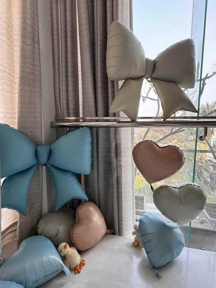 Soft pastel blue and cream bow and heart shaped foil balloons by a window