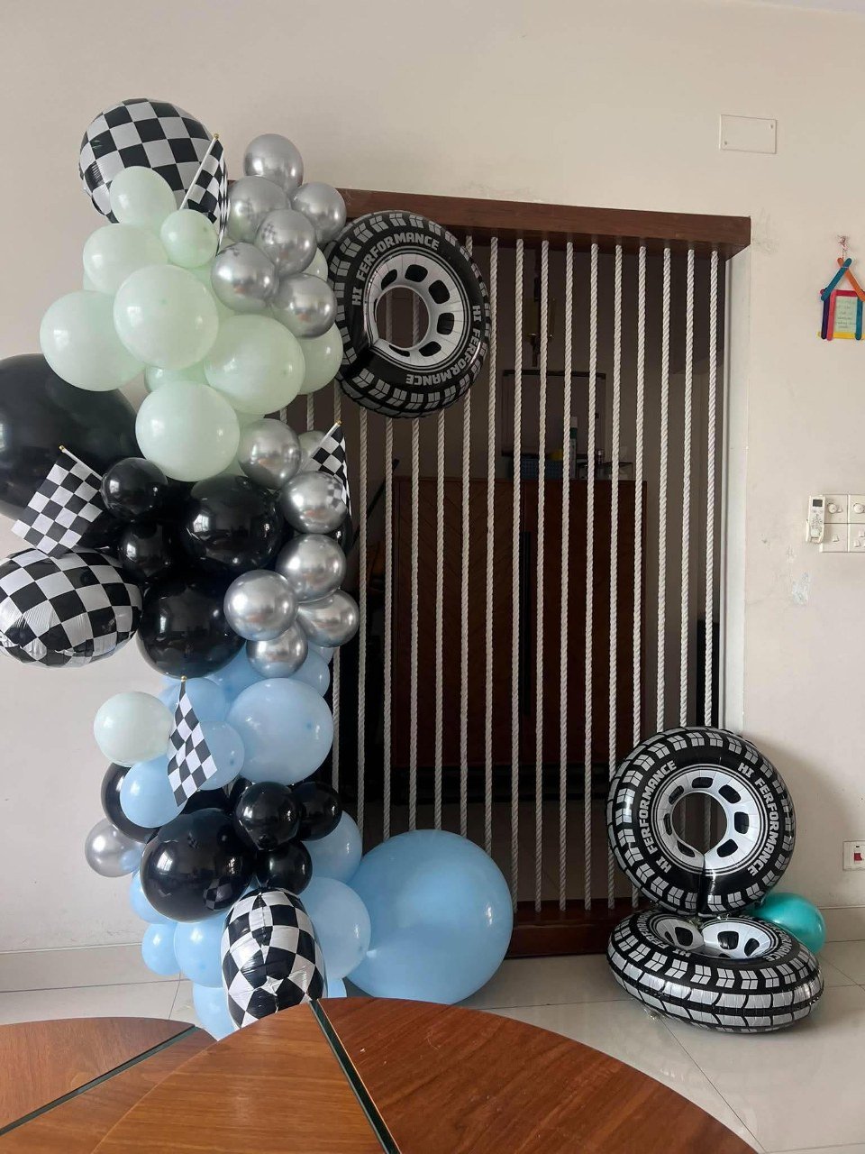 Racing themed birthday balloon garland in baby blue, mint, black and silver with checkered flags and tyre foil balloons