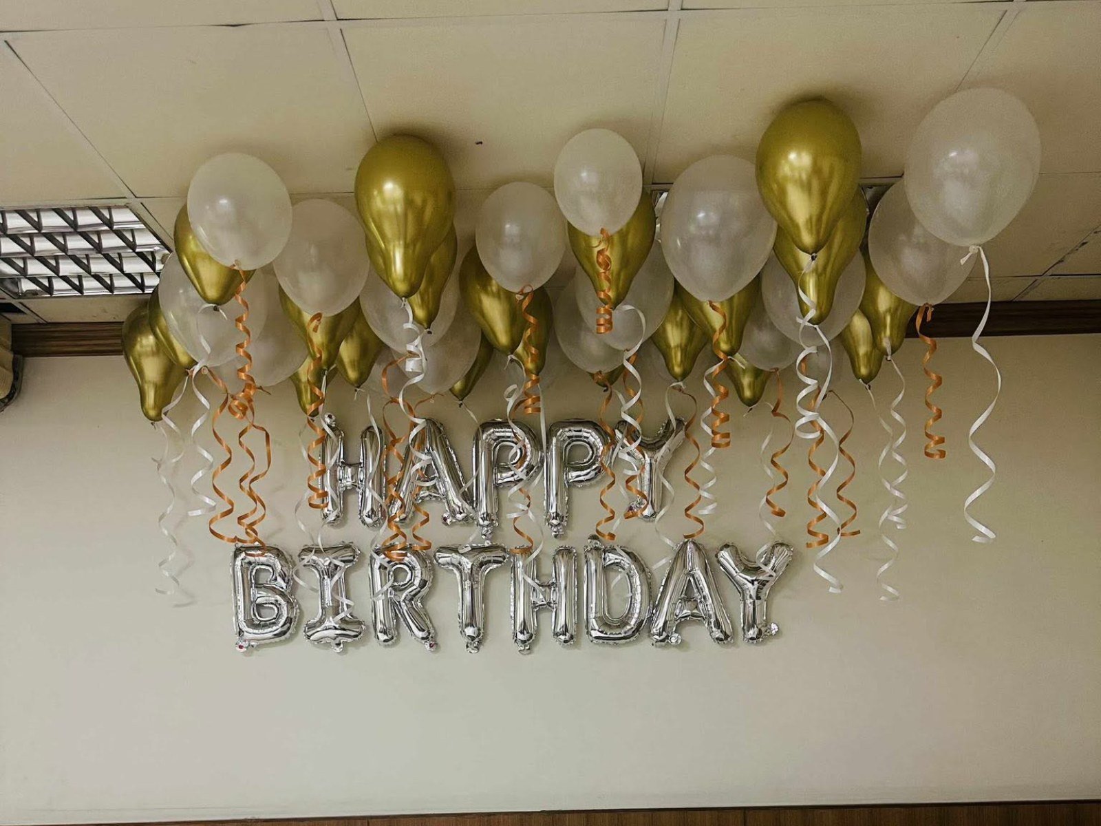 Silver Happy Birthday letter balloons with gold and white balloons on the ceiling